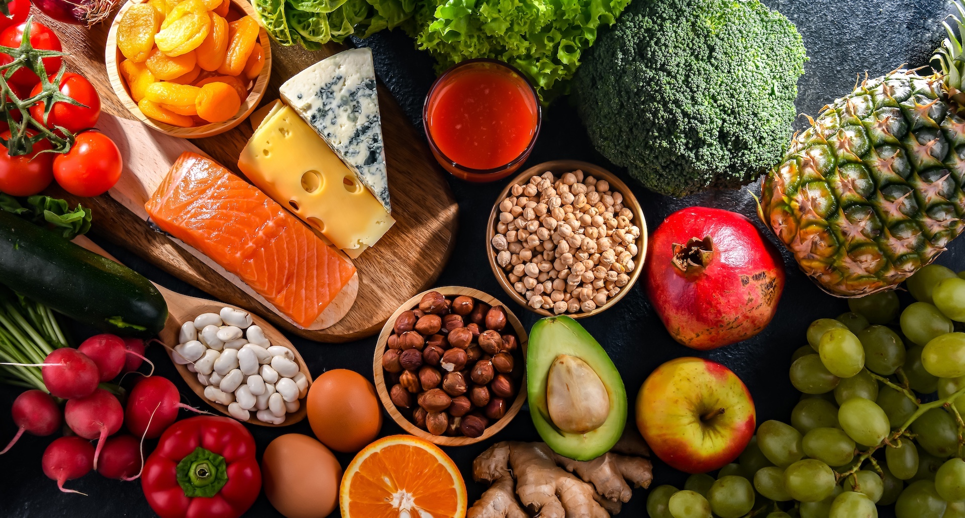 Verschiedene gesunde Lebensmittel auf einem Tisch: Gemüse, Obst, Nüsse und Käse.